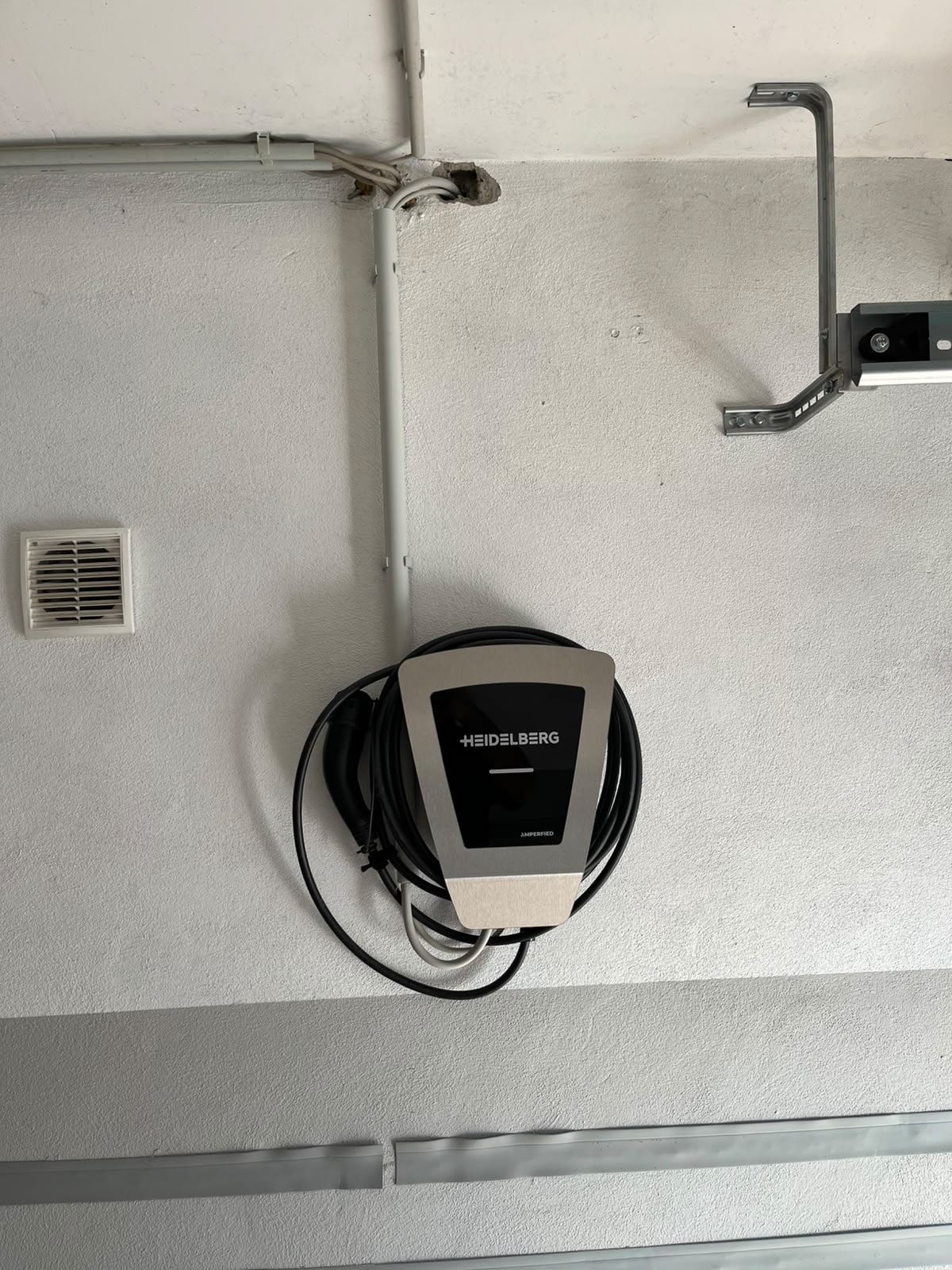 Montierte Wallbox mit aufgewickeltem Ladekabel an einer Garagenwand, Zuleitung im Installationsrohr